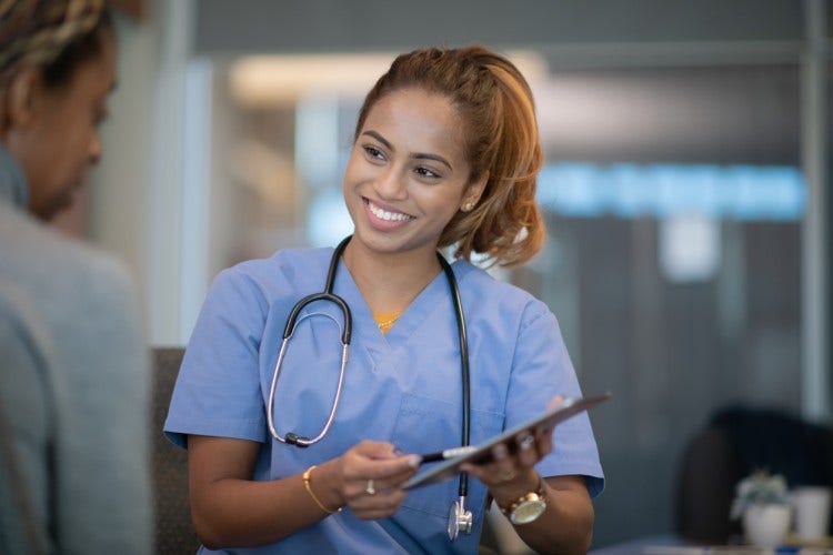 A smiling APRN shows a patient a document on a tablet.
