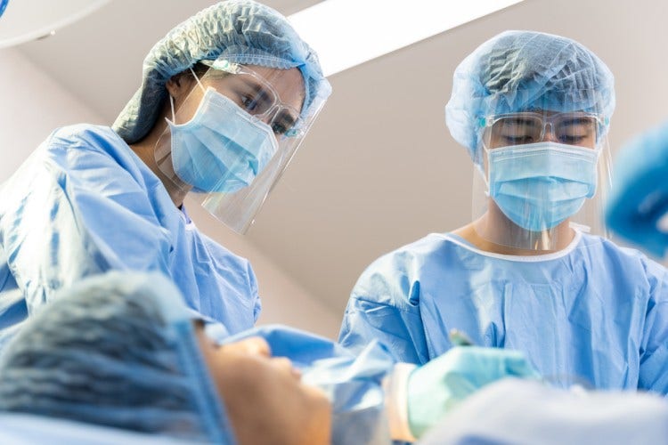An NP and an MD in masks and protective clothing attend to a patient.