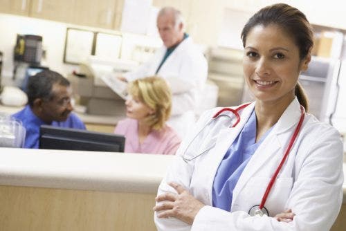 Smiling director of nursing stands in front of a busy nursing station in the hospital.