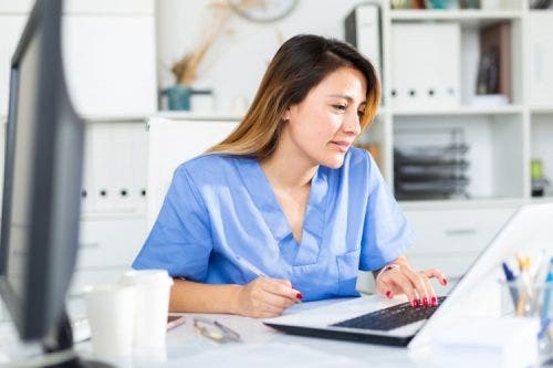 A nurse in a nurse residency program works in a hospital on a laptop.