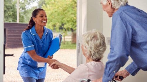A smiling nurse entrepreneur shakes hands with a patient at the door of a home.