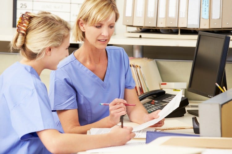 Two nurses review a document at a nurses’ station.