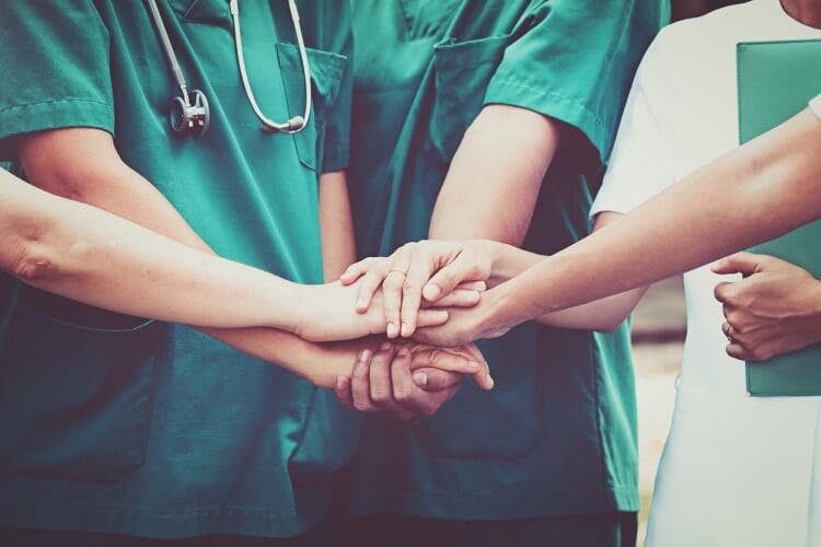 A group of health care workers huddle with their hands stacked together.