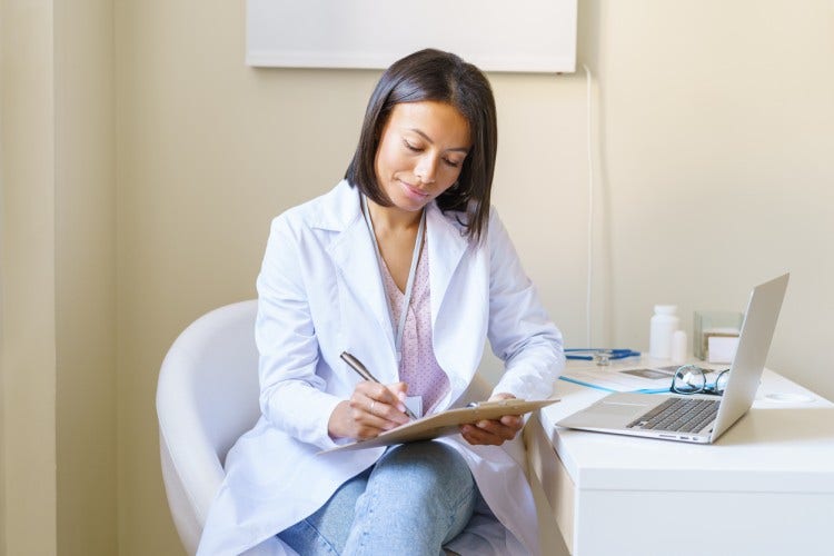 An informatics nurse works at a desk with a tablet and laptop.
