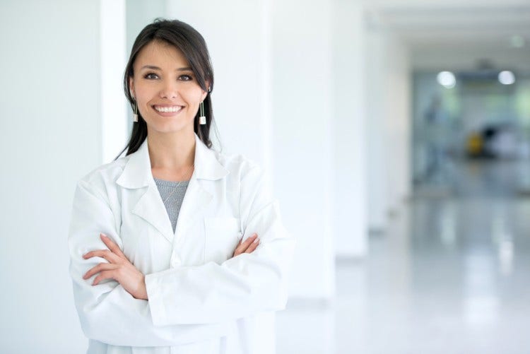 A smiling nurse practitioner in a hospital hallway.