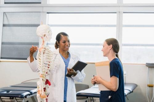 A nurse educator points to a skeleton while talking with a student.