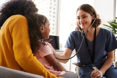 A smiling family nurse practitioner checks the vital signs of a child sitting on a parent’s lap.