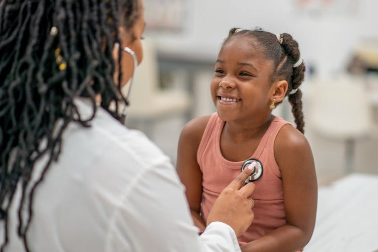 An FNP listens to a young patient’s heart with a stethoscope.