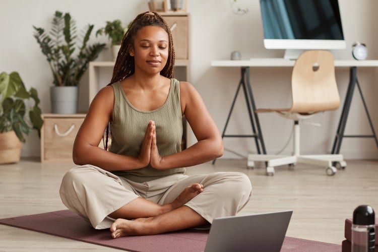 A person is sitting with legs crossed and eyes closed while practicing meditation in a home office.