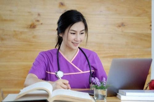 Nursing student studying at a desk with books and a laptop.